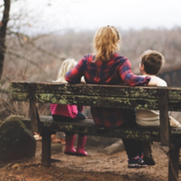 Eine Mutter sitzt mit ihren zwei Kindern auf einer Bank und schaut in die Ferne. 