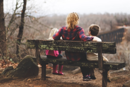 Eine Mutter sitzt mit ihren zwei Kindern auf einer Bank und schaut in die Ferne. 