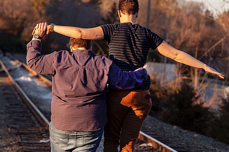 Zwei Personen gehen Hand in Hand an Bahngleisen entlang.