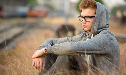 Junge sitzt auf Feld. Er guckt nachdenklich und trägt einen Kapuzenpullover.