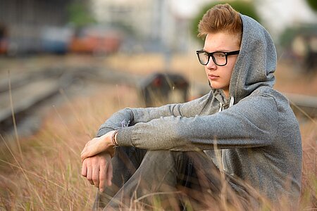 Junge sitzt auf Feld. Er guckt nachdenklich und trägt einen Kapuzenpullover.