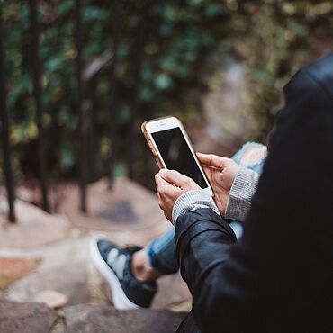 Eine Person sitzt auf einer Treppe und hält ein Handy in der Hand.