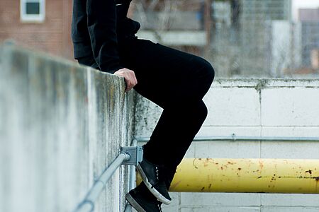 Junge sitzt auf einer Mauer und lässt die Beine baumeln.